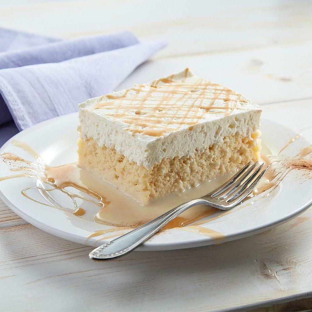 A slice of tres leches cake with whipped cream and caramel on a white plate